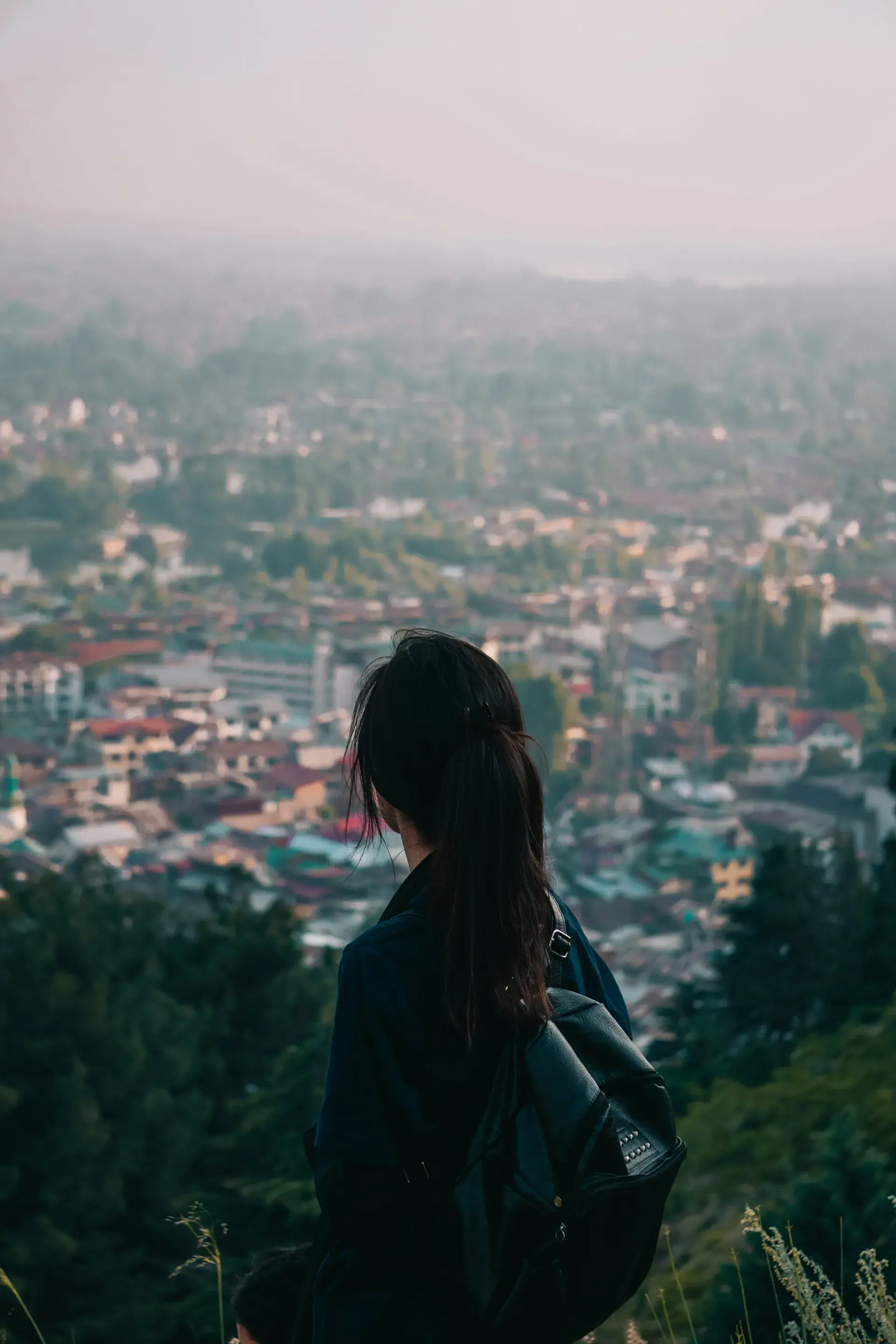 Estudiante con mochila contemplando una ciudad europea al atardecer desde una colina